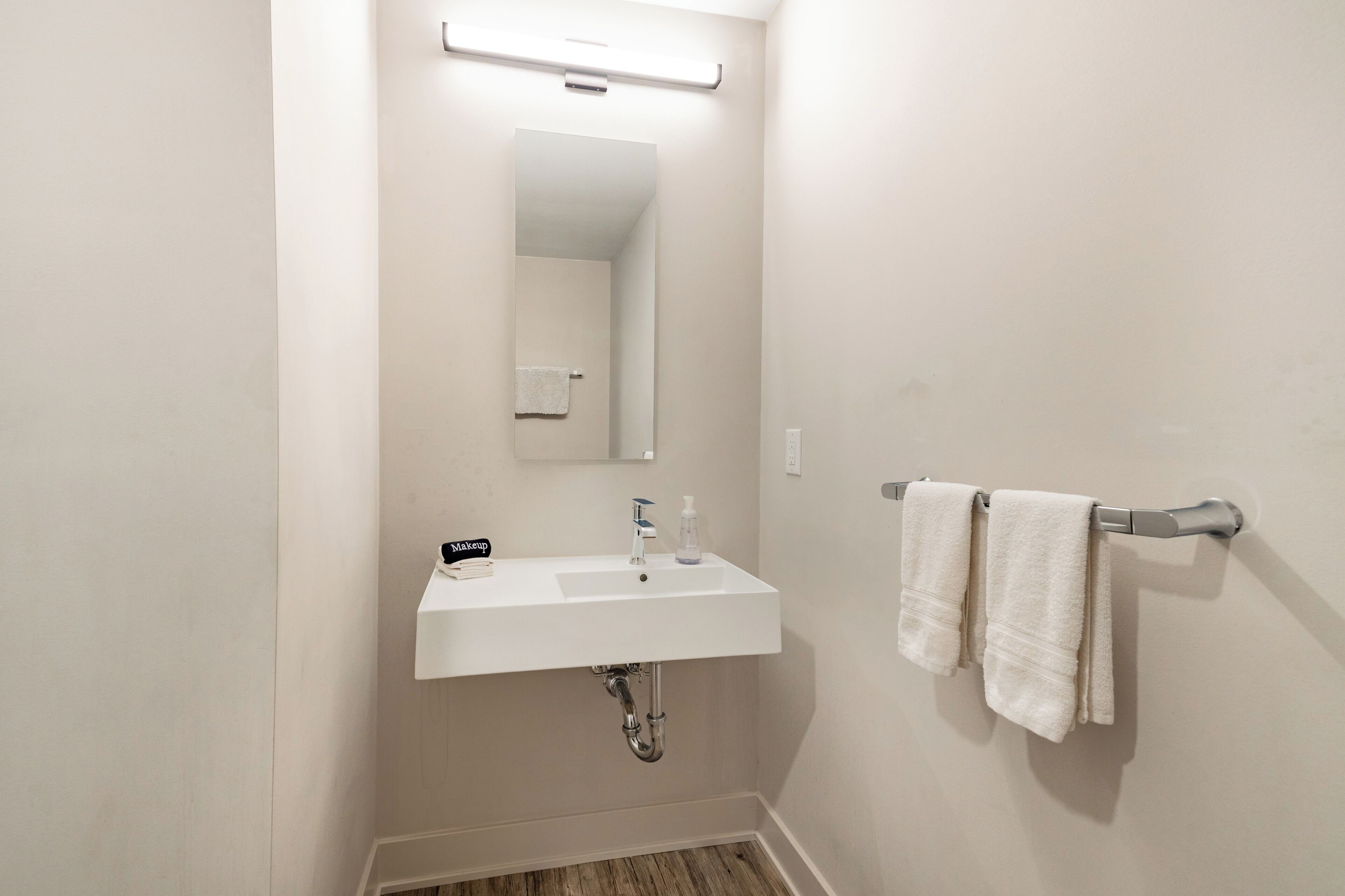 Een badkamer met een witte wastafel, een spiegel en een handdoekrek met twee handdoeken.