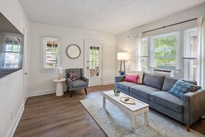 A living room with a grey sofa, a small armchair, a white coffee table, and a patterned rug. - The Retreat - Warm and Convenient Guest Suite (Cincinnati)