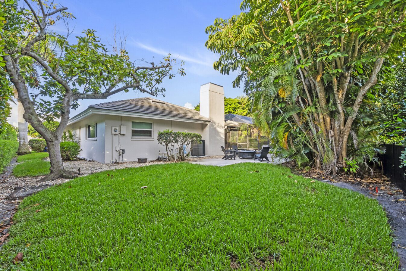 A single-story house with a covered patio, a lawn, and a variety of trees and shrubs.