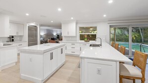 Une cuisine moderne avec des meubles blancs, un grand îlot central et une vue sur une piscine.