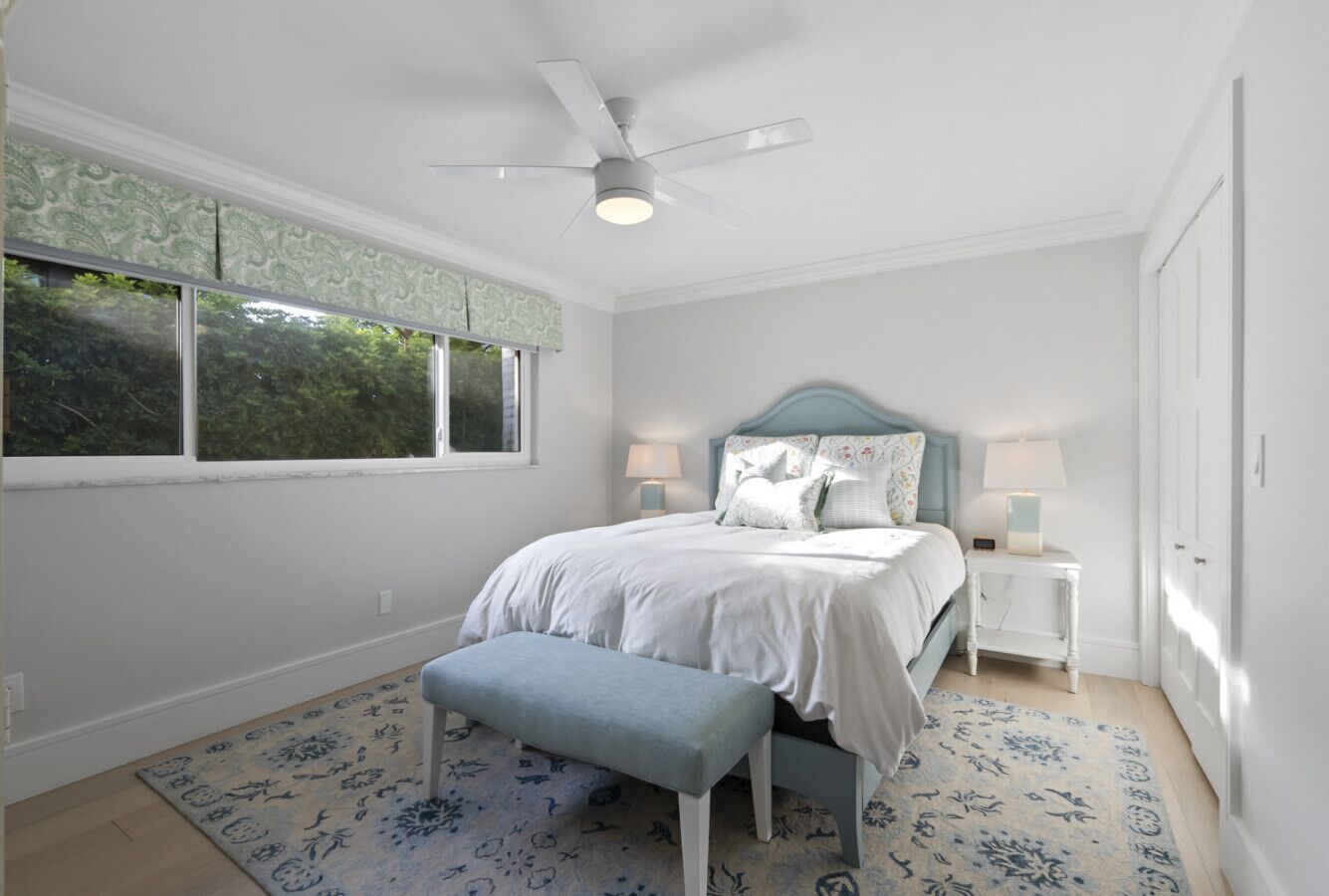 A bedroom with a bed, a bench, a ceiling fan, and two bedside tables with lamps.