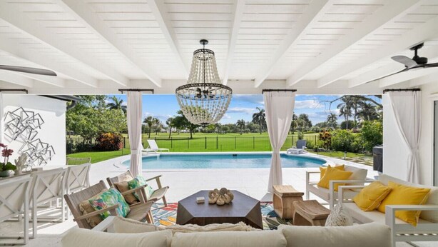 Un espace extérieur aménagé, abrité, avec une piscine, des meubles blancs et un lustre décoratif.