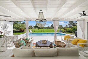 A covered outdoor seating area with a pool, white furniture, and a decorative chandelier. - Luxury Beach House With Golf Course View (Naples)