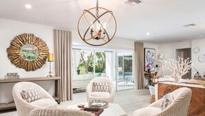 Un salon moderne avec un lustre, deux fauteuils, une table basse et une vue sur l’extérieur.