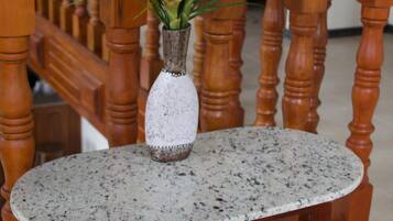 Une table ronde avec un plateau à motifs, un vase blanc orné d’un motif décoratif et une plante aux fleurs jaunes et aux feuilles vertes.