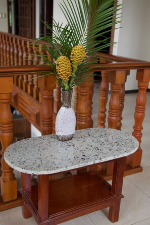 Una mesa redonda con una superficie moteada, un jarrón blanco con un diseño decorativo y una planta con flores amarillas y hojas verdes.