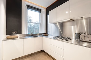 A modern kitchen with white cabinets, a stainless steel range hood, a gas stove, and a toaster. - Exclusive Cadogan Square Private Elevator (London)