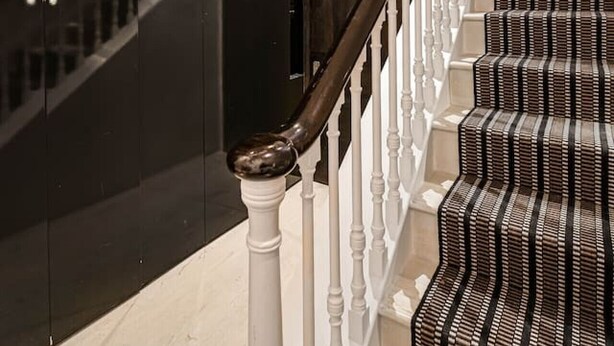 A staircase with a dark wooden handrail and white balusters, leading to a dark wall with a door. - Cadogan Square 3BR Prime Location (London)