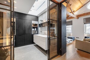 A modern kitchen with dark cabinetry, a white countertop, and a glass door leading to a dining area. - Cadogan Square Penthouse Huge Terrace AC (London)