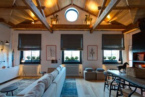 A spacious living room with a high ceiling, wooden beams, a large round skylight, and a cozy seating area with a sofa and a dining table. - Cadogan Square Penthouse Huge Terrace AC (London)