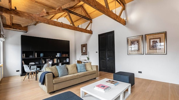 A spacious living room with a high ceiling, wooden beams, a sofa, a coffee table, and a bookshelf. - Cadogan Square Penthouse Huge Terrace AC (London)