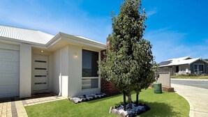 A modern single-story house with a garage, a well-maintained lawn, and a large tree in front. - Spacious 3-Bed Home in Peaceful Byford (Byford)
