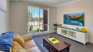 A living room with a sofa, a coffee table, a TV, and a painting. - Spacious 3-Bed Home in Peaceful Byford (Byford)