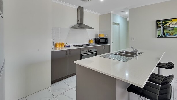 A modern kitchen with a central island, stainless steel appliances, and a large window. - Spacious 3-Bed Home in Peaceful Byford (Byford)
