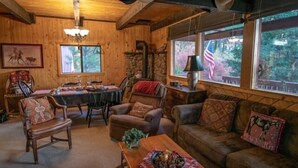 En mysig stuga med en matplats, en öppen spis och stora fönster som ger utsikt över skogen.