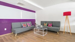 Ett modernt vardagsrum med en grå soffa, färgglada kuddar, ett vitt soffbord och en röd golvlampa.