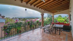 Eine überdachte Terrasse im Freien mit Tisch, Stühlen und einer Hängematte, mit Blick auf die umliegende Landschaft.