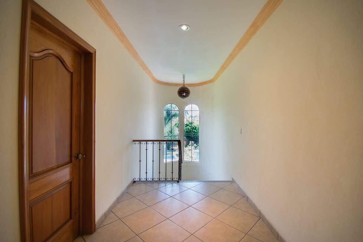 A hallway with a wooden door, a metal gate, and a view of greenery through a window.