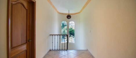 A hallway with a wooden door, a metal gate, and a view of greenery through a window.