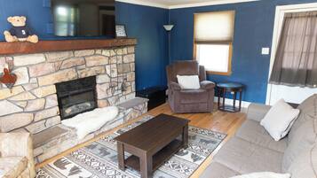 A living room with a stone fireplace, a brown sofa, a brown armchair, a small round table, and a patterned rug.