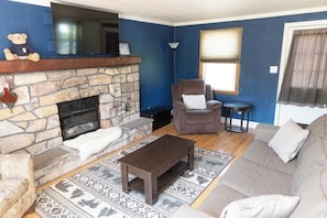 A living room with a stone fireplace, a brown sofa, a brown armchair, a small round table, and a patterned rug. - Close to Stadium, Hot Tub, Private Fishing!
3-bedroom house in State College (State College)