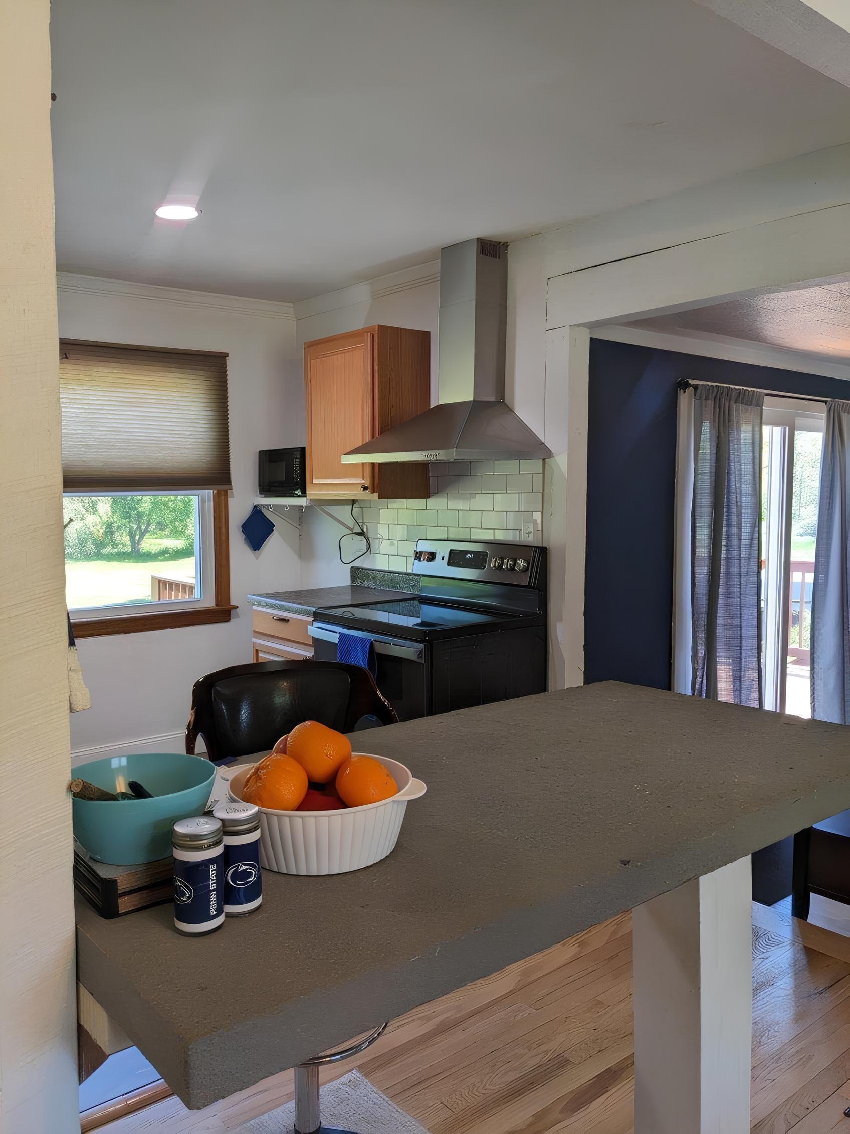 A compact kitchen with a built-in stove, a microwave, and wooden cabinets. A bowl of oranges and a blue bowl are on the counter.