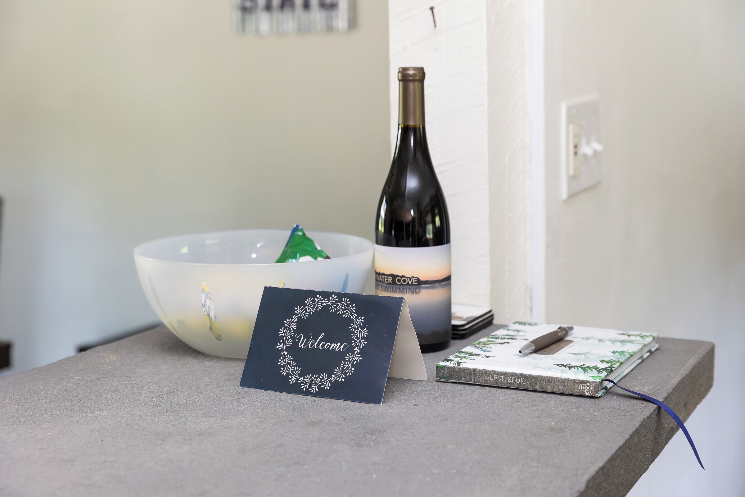 A welcome card, a bottle of wine, a notebook, and a pen on a table.