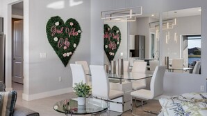 Uma sala de jantar moderna com mesa de vidro, cadeiras brancas e arte decorativa na parede em formato de coração com a inscrição 