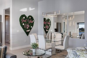 A modern dining area with a glass table, white chairs, and decorative heart-shaped wall art with the text "Good Vibes Only". - Elite Sunset Oasis | Heated Pool/Spa | Game Room (Cape Coral)