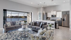 Uma sala de estar moderna e aberta, com grandes janelas com vista para a água, cozinha com eletrodomésticos de aço inoxidável e área de jantar com mesa de vidro.