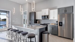 Cozinha moderna com ilha central, banquetas, eletrodomésticos de aço inoxidável e vista para a água.