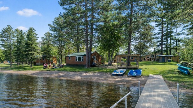 Un chalet au bord du lac, avec un quai, des bateaux et une zone herbeuse bordée d’arbres.
