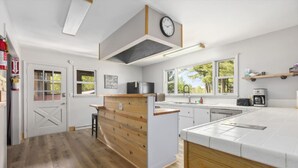 Une cuisine moderne avec un îlot central en bois, des meubles blancs et une horloge au mur.