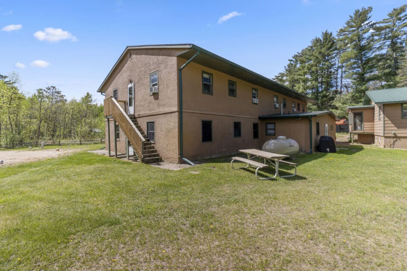A two-story building with a staircase leading to the entrance, a picnic table, and a large water tank in the yard.