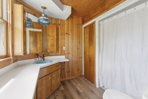 A wooden-paneled bathroom with a white sink, wooden cabinets, and a shower curtain. - Perfect Lake Escape | Sleeps 14 | Water views! (Emily)