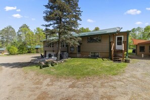 A two-story building with a green roof, a covered outdoor seating area, and a staircase leading to the entrance. - Perfect Lake Escape | Sleeps 14 | Water views! (Emily)