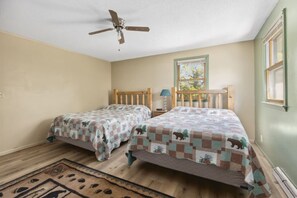 A bedroom with two beds, a ceiling fan, a window, and a nightstand with a lamp. - Perfect Lake Escape | Sleeps 14 | Water views! (Emily)