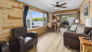 A cabin with a dining area, a sofa, and a view of a lake. - Cozy Cottage Steps From the Water (Emily)