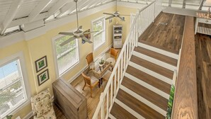 Um quarto espaçoso com teto alto, área de jantar com mesa e cadeiras, escada com degraus de madeira e um ventilador de teto.