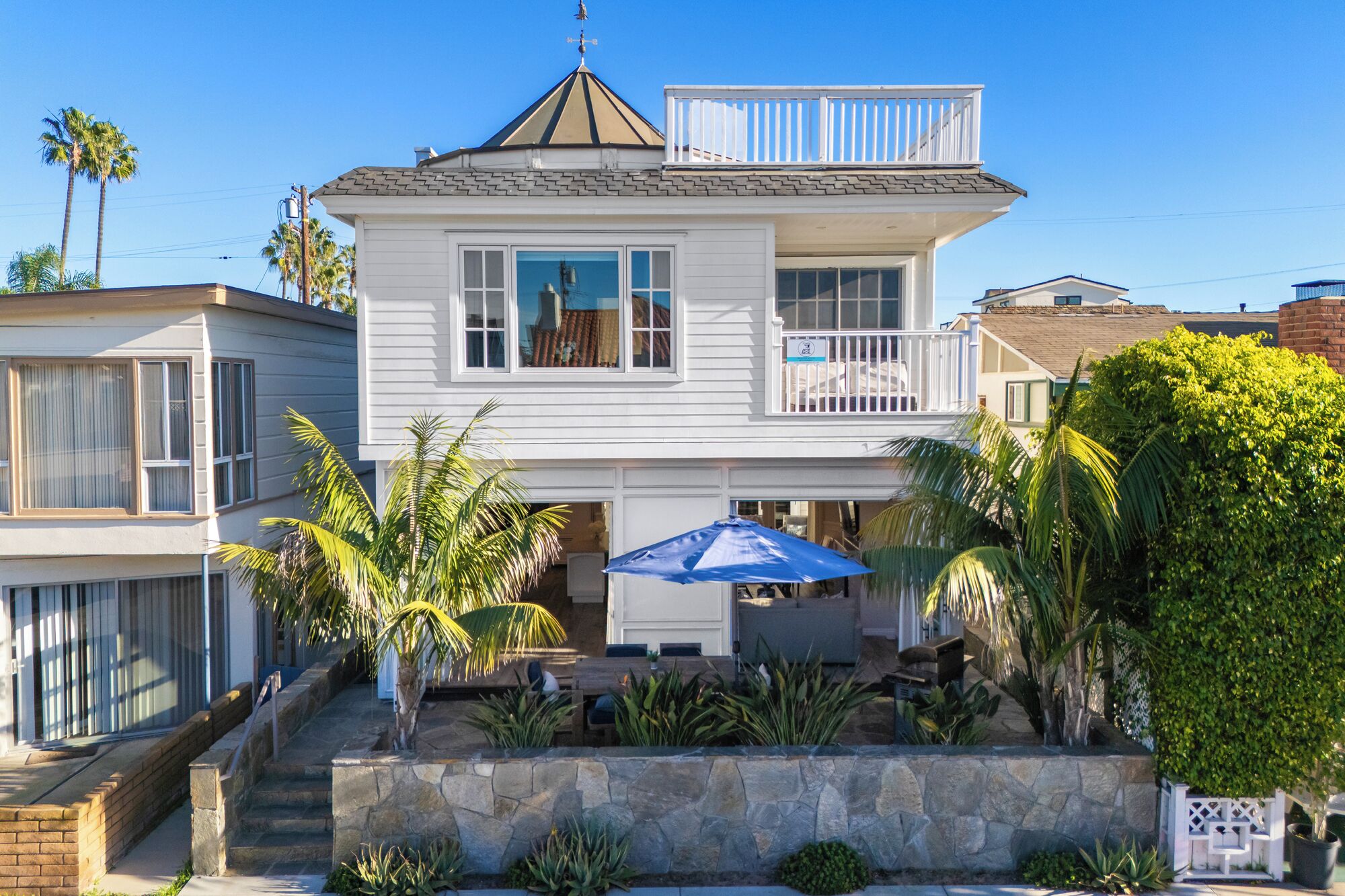 Une maison à deux étages dotée d  ’un balcon, d’un escalier en pierre et d’un patio aménagé avec du mobilier d’extérieur.