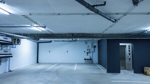 Eine leere Tiefgarage mit Betonböden, weißen Wänden und einem Metallaufzug.