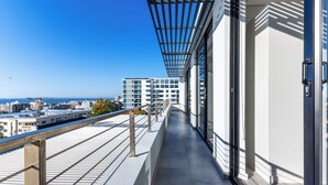 Ein Balkon mit Blick auf Stadt und Meer, ausgestattet mit einem modernen Geländer und einer Glastür.