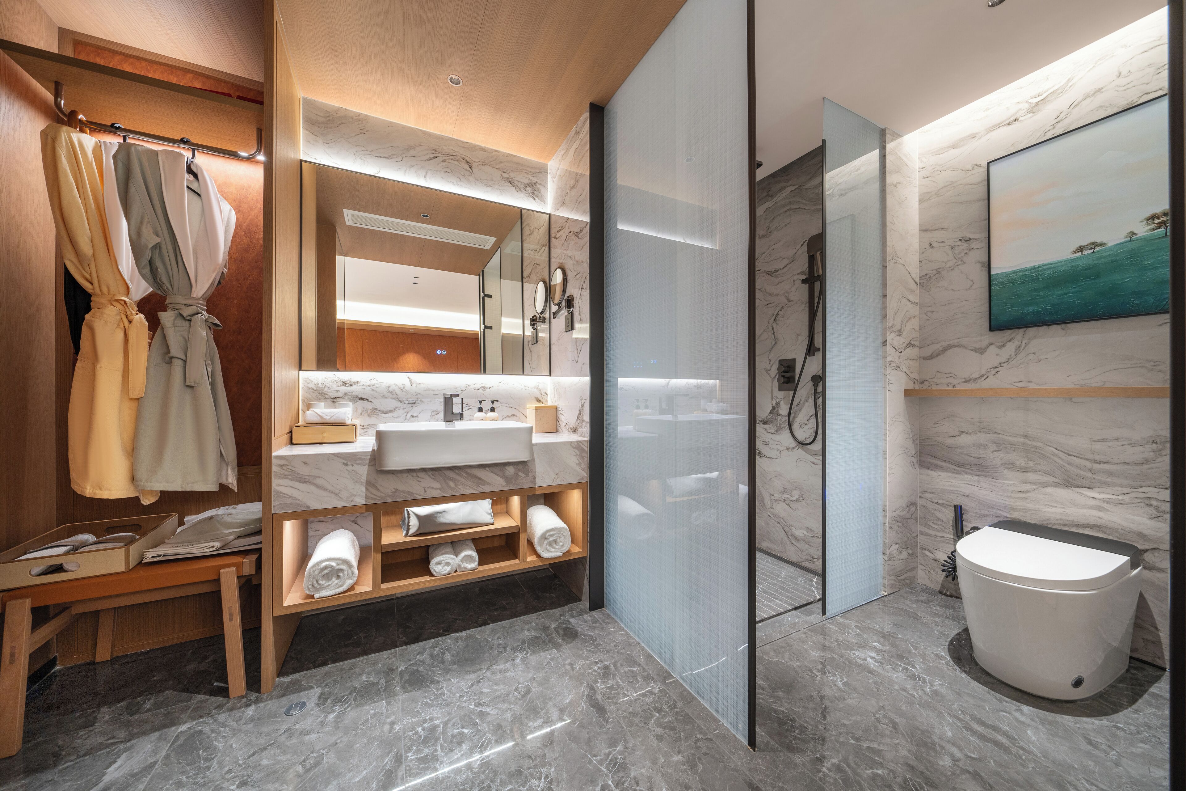 Un baño moderno con tocador de mármol, cabina de ducha con mampara de vidrio y tocador de madera con toallas y artículos de aseo.