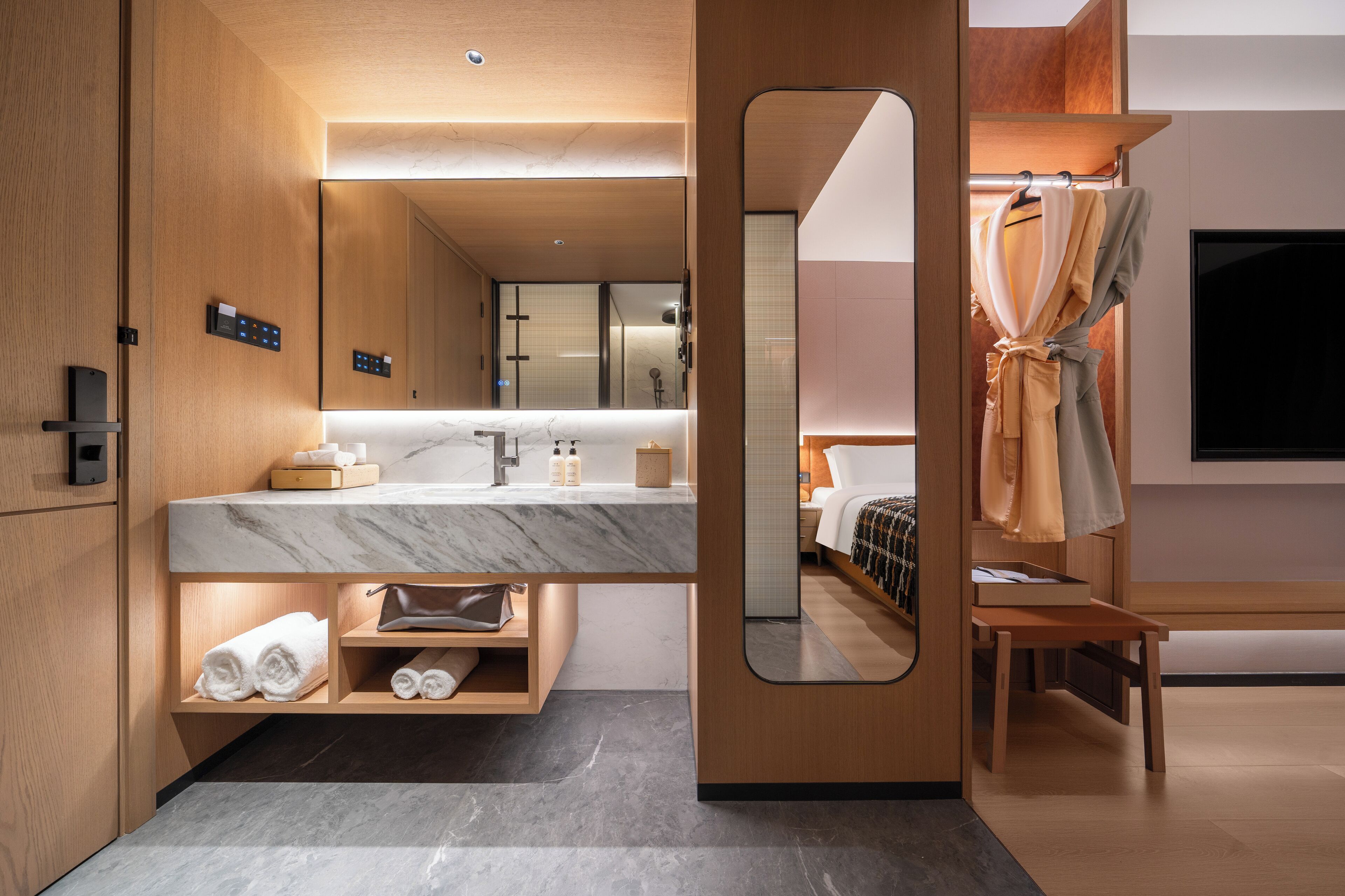 A modern hotel bathroom with a marble countertop, wooden vanity, a large mirror, and a shower area.