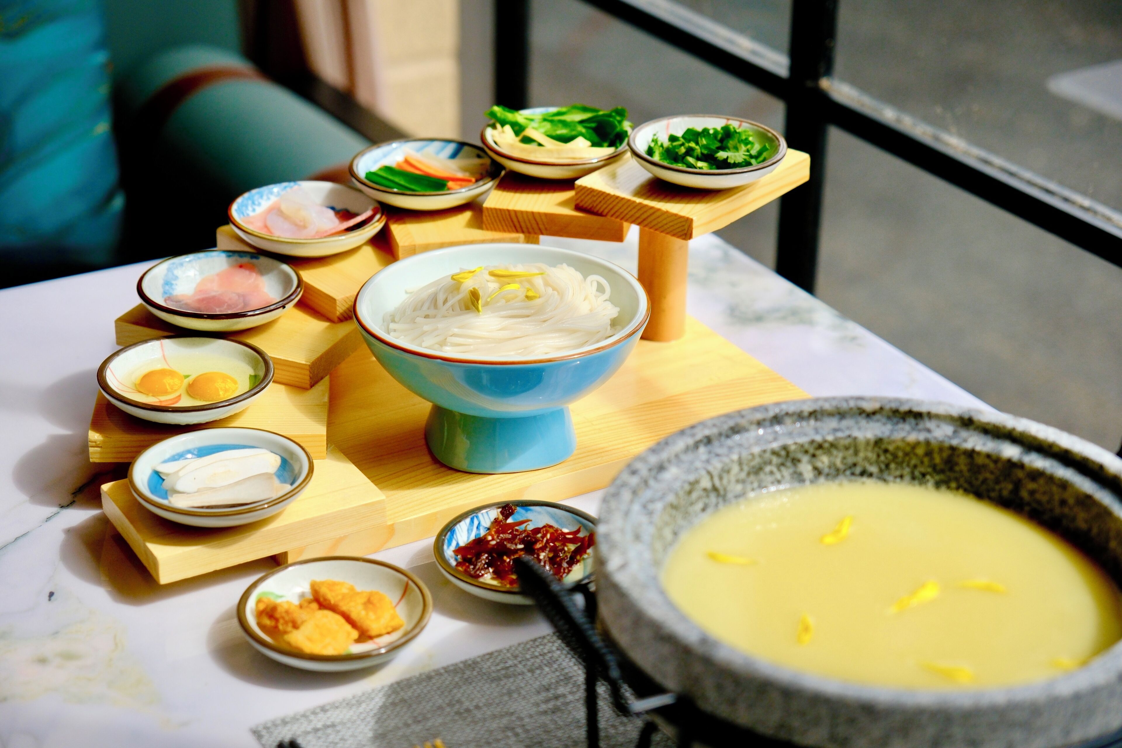 A table with various dishes, including a bowl of noodles, a bowl of soup, and several small dishes with different foods.