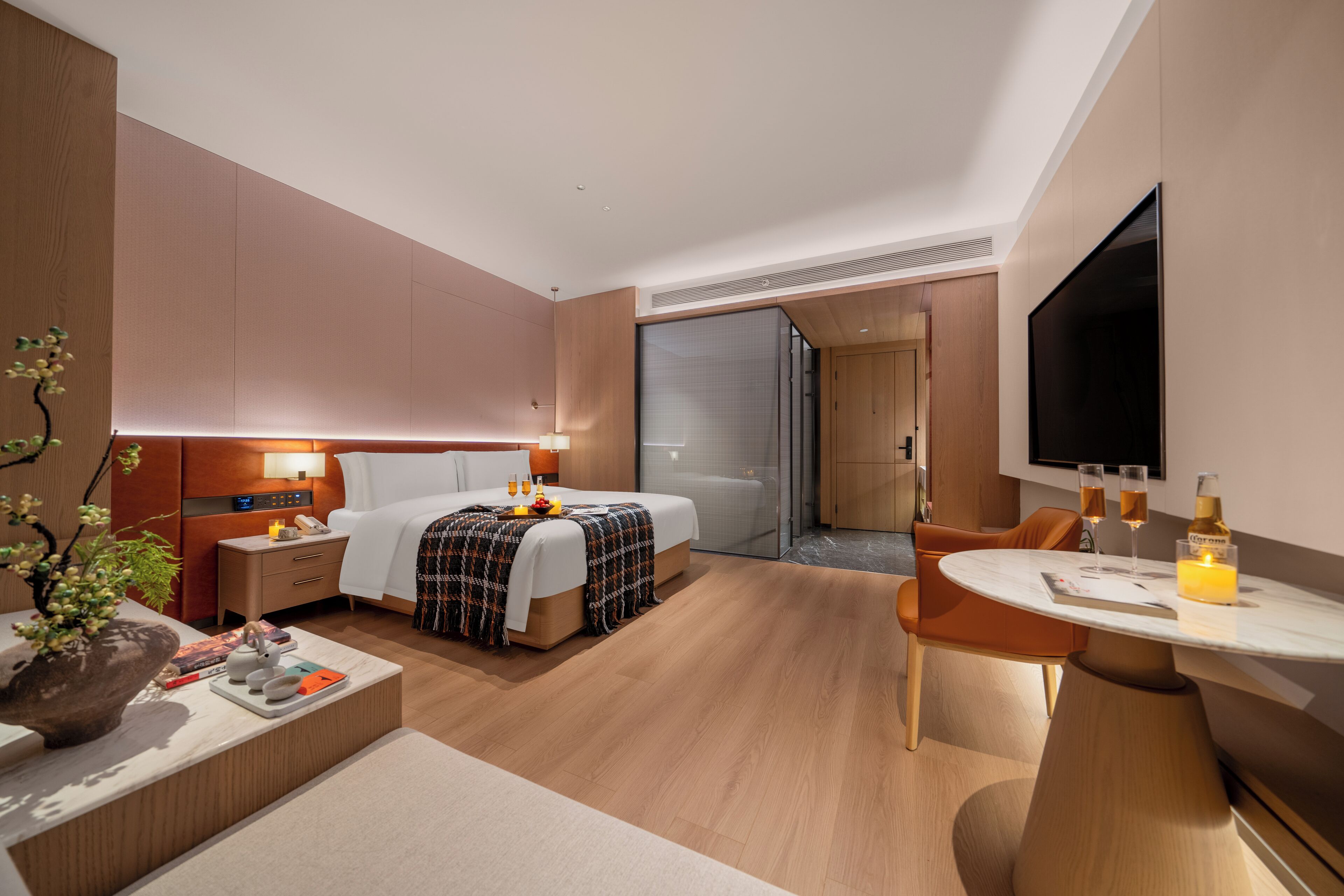 Una habitación de hotel moderna con cama, mesita de noche, lámpara y un pequeño comedor con mesa y sillas.