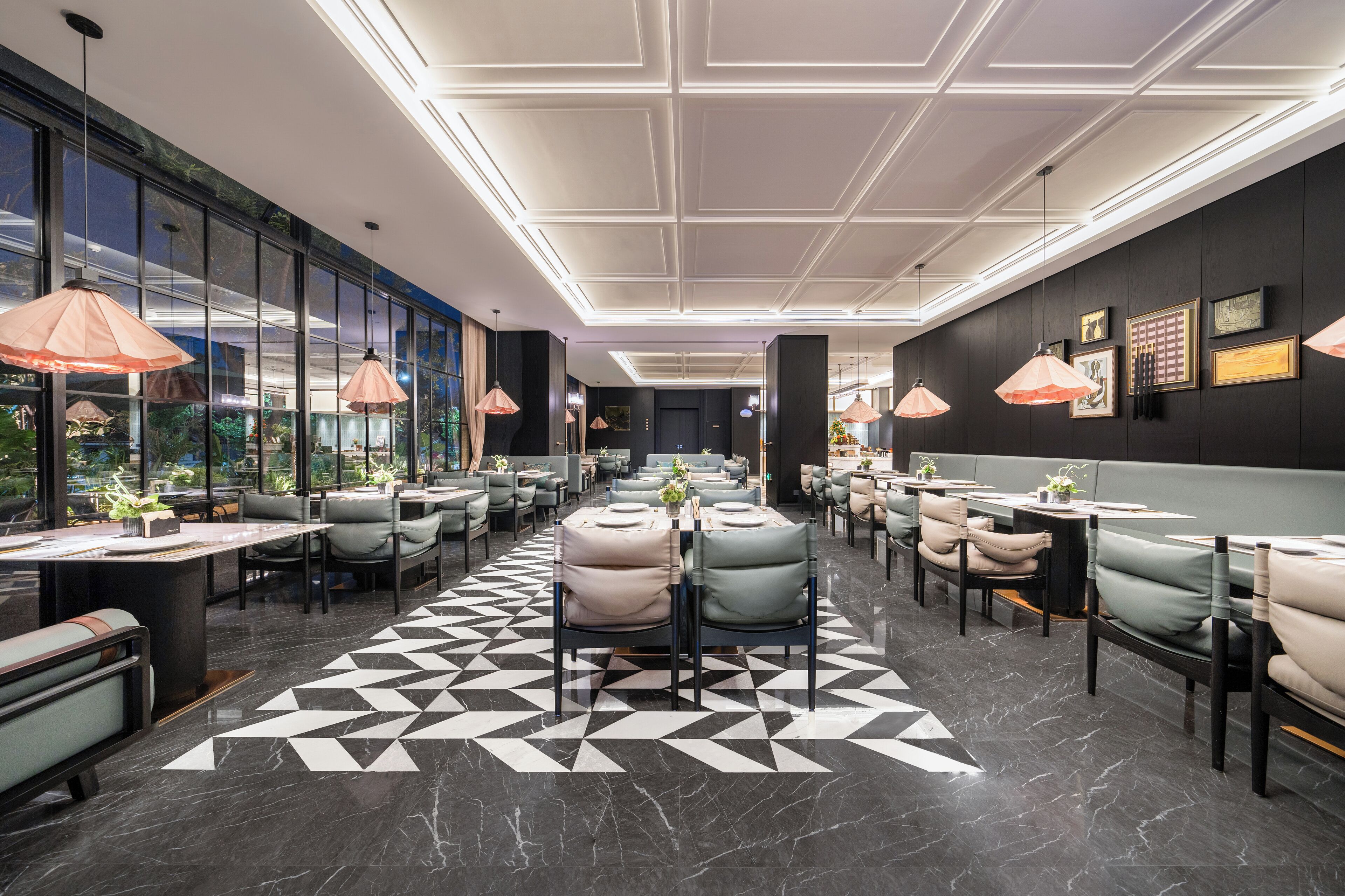 Un restaurant moderne avec un motif géométrique sur le sol, des luminaires suspendus et une vue dégagée grâce à de grandes fenêtres.