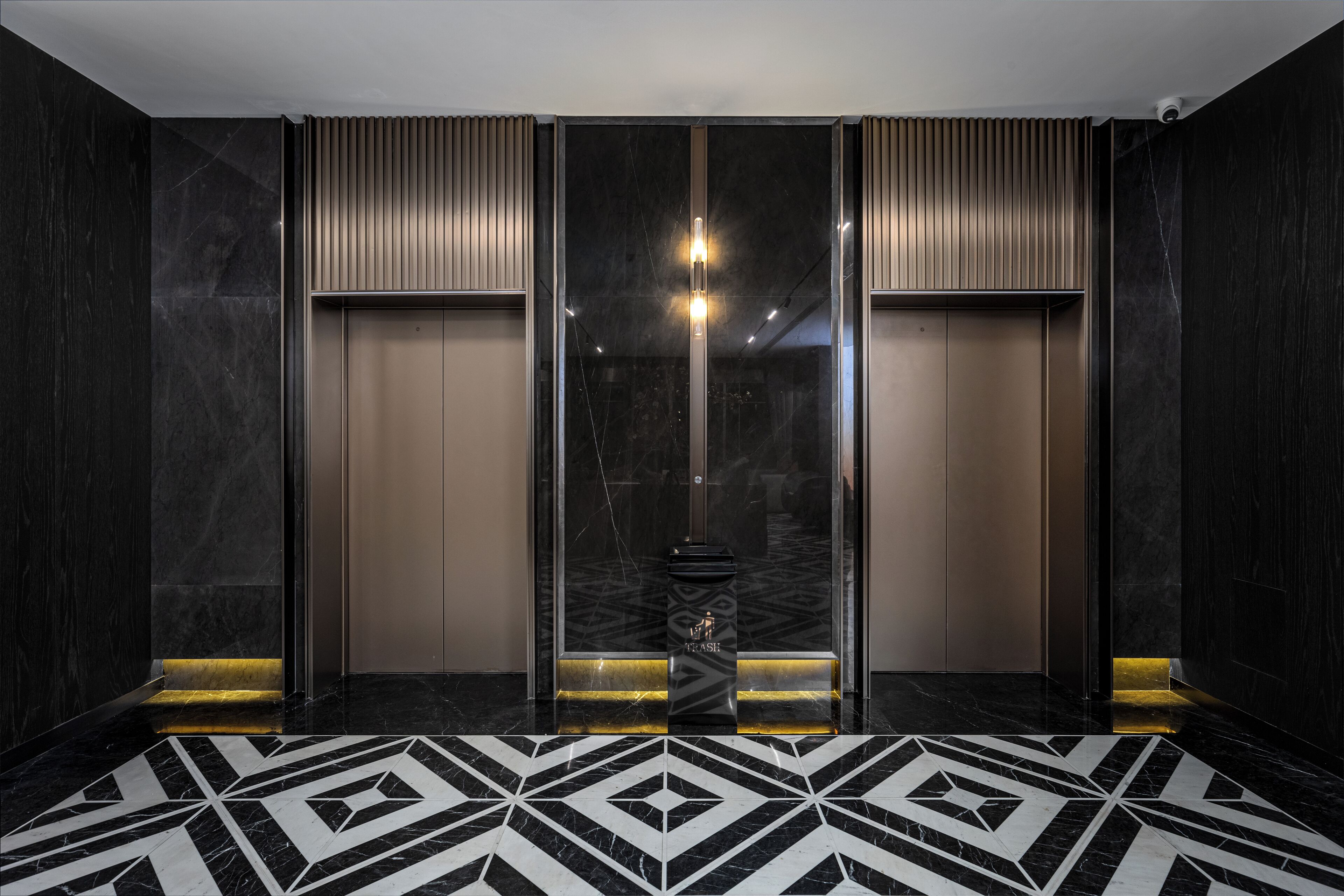 A modern elevator with a geometric patterned floor, a central light fixture, and a trash bin.