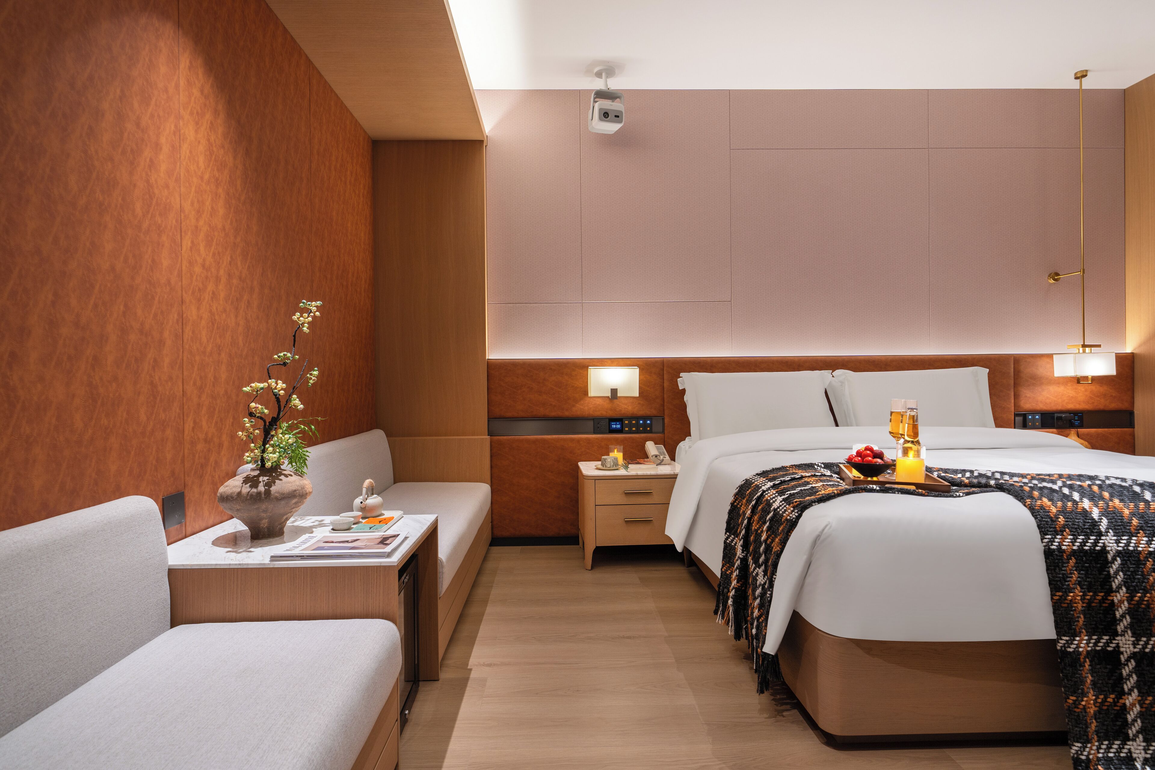 A hotel room with a bed, bedside table, lamp, and a small desk with a chair.