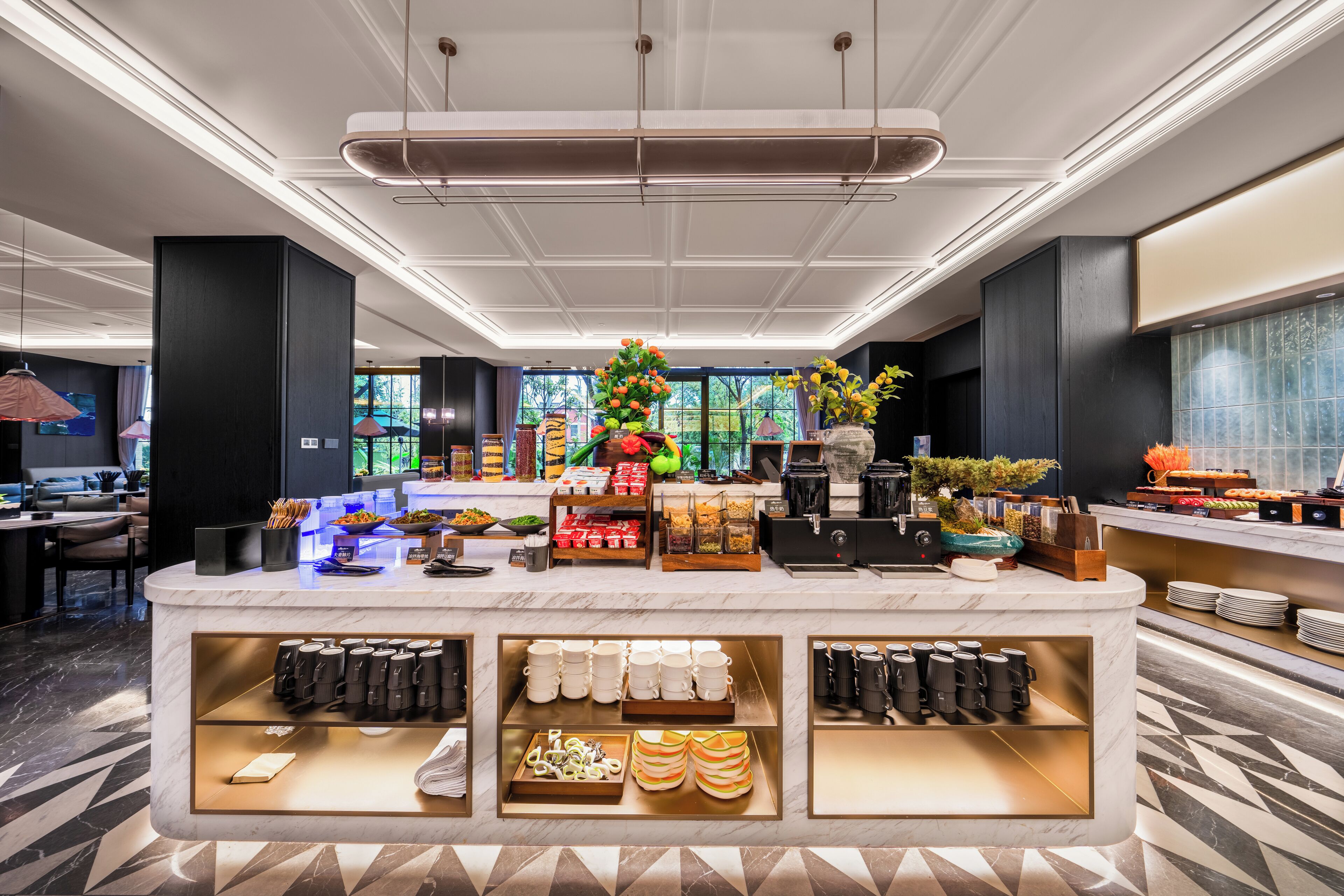 A modern hotel lobby with a marble reception desk, a coffee station, and a seating area with a view of the outdoors.